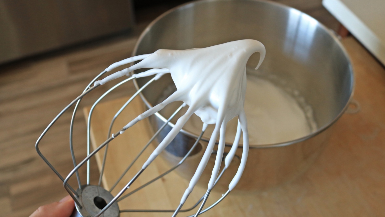 A whisk with whipped aquafaba on it.