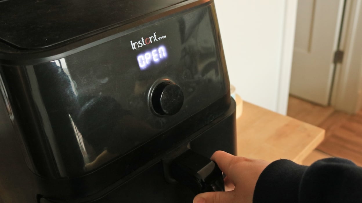 A hand opening the basket of the Instant Vortex air fryer.