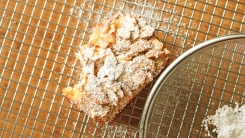A slice of pound cake with almond topping on a cutting board.