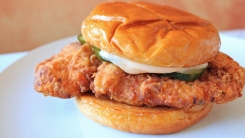 A copycat Popeyes fried chicken sandwich with pickles on a white plate.