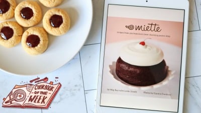 A cookbook on an ipad next to a plate of raspberry thumbprint cookies.